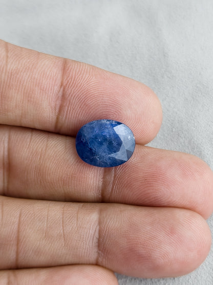Face-up oval blue sapphire resting on fingers for a size reference.
