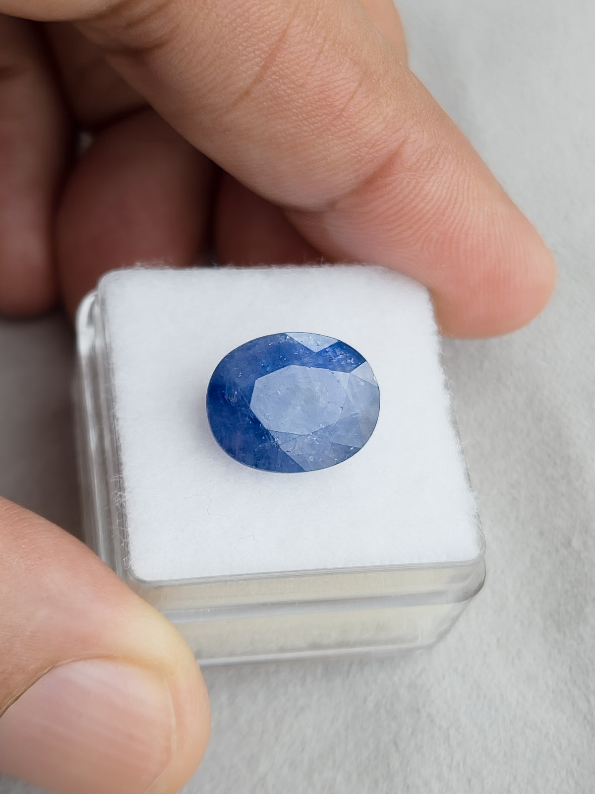 Face-up oval blue sapphire resting on a white display pad held in a hand.