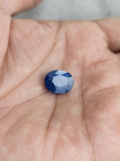 The loose oval blue sapphire resting face-up in a palm to show its scale.