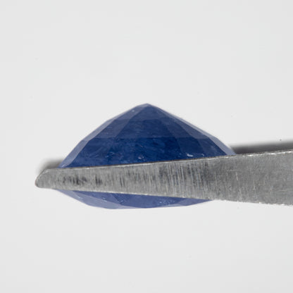 Side profile of the oval blue sapphire held in tweezers, showing crown and pavilion depth.