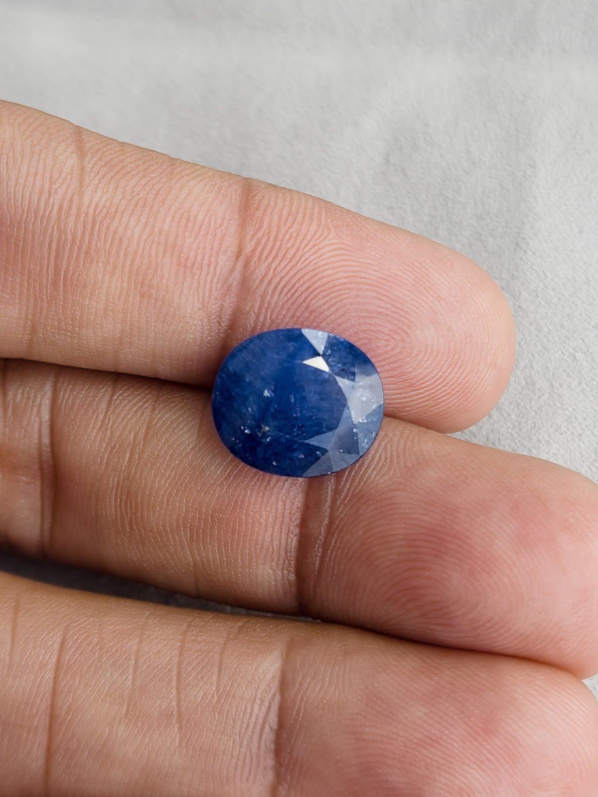 Face-up oval blue sapphire resting on fingers for a size reference.