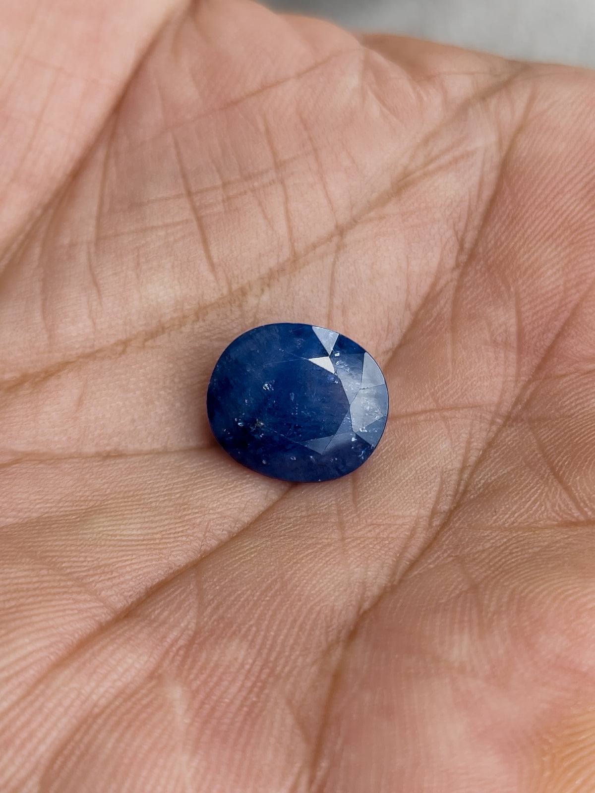 The loose oval blue sapphire resting face-up in a palm to show its scale.