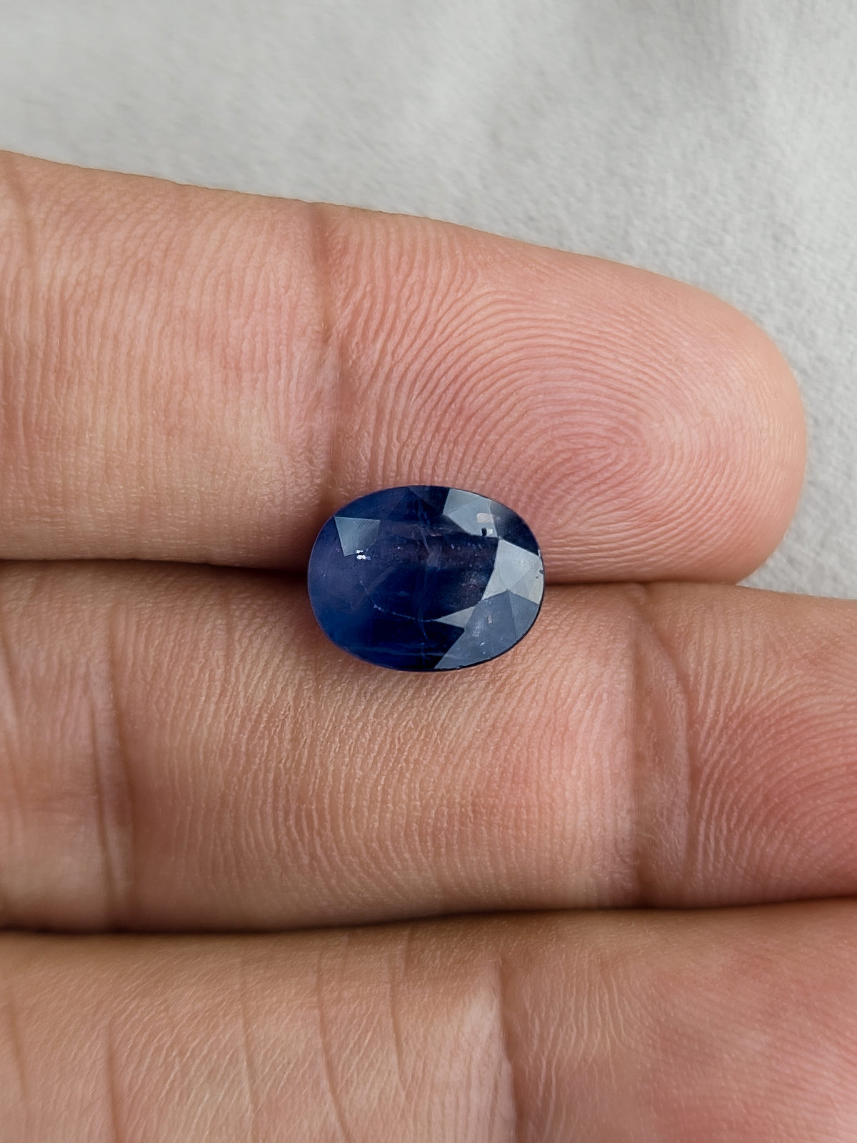 Face-up oval blue sapphire resting on fingers for a size reference.