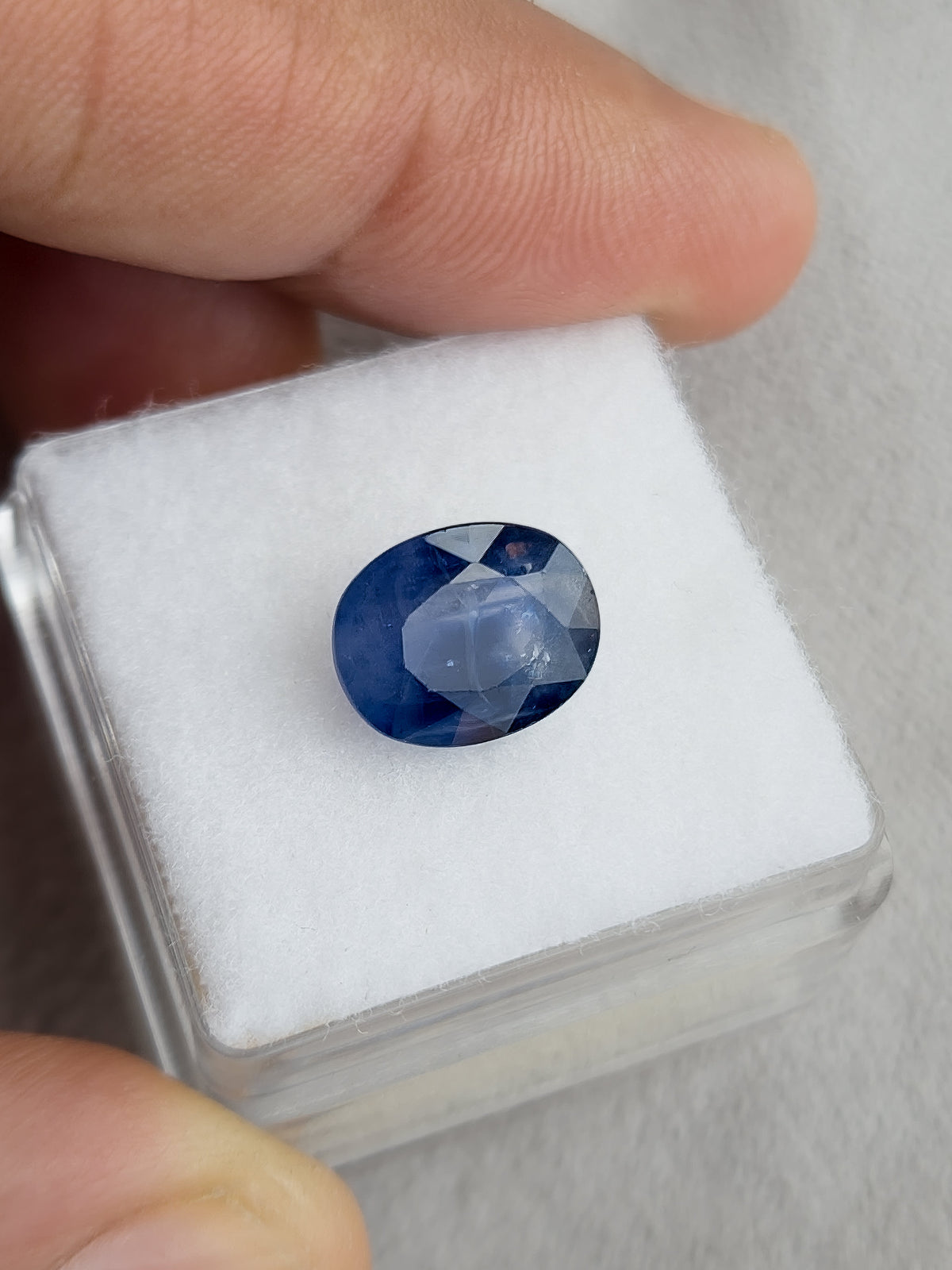 Face-up oval blue sapphire resting on a white display pad held in a hand.