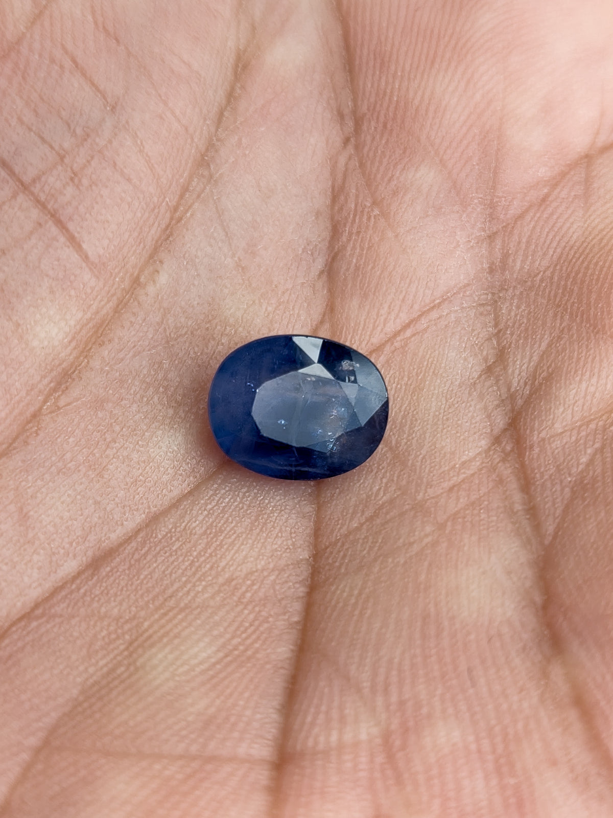 The loose oval blue sapphire resting face-up in a palm to show its scale.